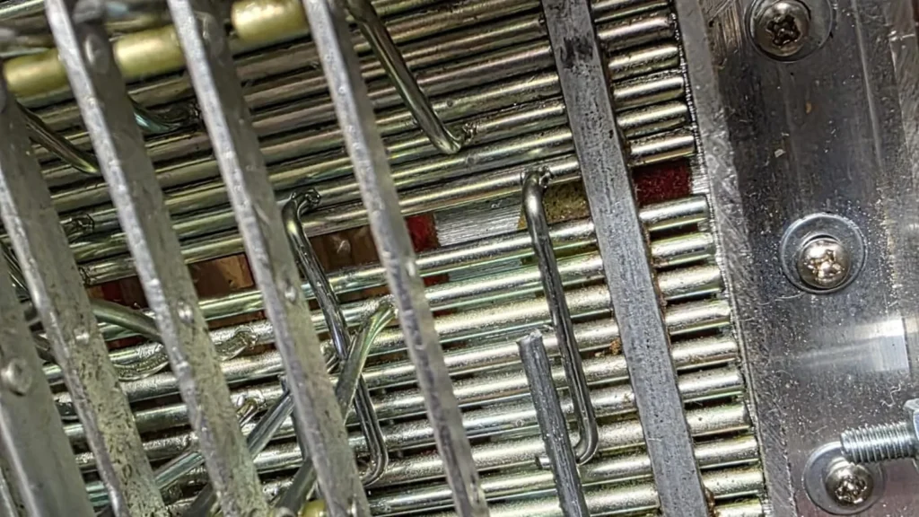 Detailaufnahme der verschmutzten Mechanik im Inneren eines Akkordeons vor der Reinigung.